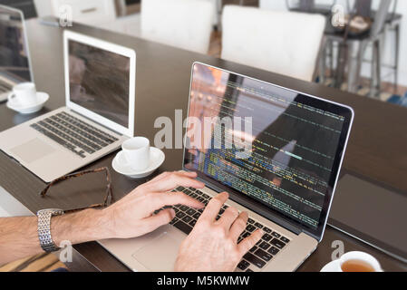 Mehrere Computer mit Kaffee in einer Büroumgebung mit Händen tippen. Stockfoto