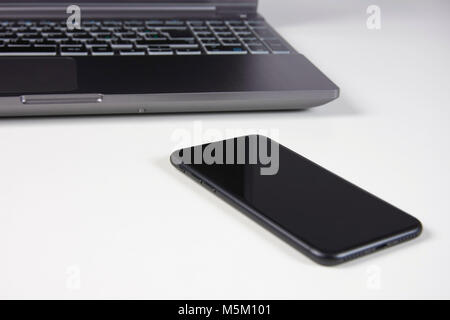 Silber Laptop und schwarz Smartphone liegen auf einem weißen Schreibtisch Tisch Stockfoto