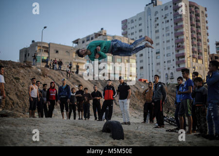 Gaza, Gaza. 23 Feb, 2018. Palästinenser beobachten, wie eine Jugend Praktiken seiner parkour Fähigkeiten auf den Strand von Gaza, Gaza, den 23. Februar 2018. Credit: Mohammed Talatene/dpa/Alamy leben Nachrichten Stockfoto