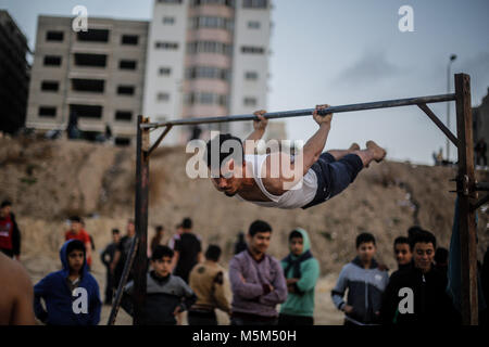 Gaza, Gaza. 23 Feb, 2018. Palästinenser beobachten, wie eine Jugend Praktiken seiner parkour Fähigkeiten auf den Strand von Gaza, Gaza, den 23. Februar 2018. Credit: Mohammed Talatene/dpa/Alamy leben Nachrichten Stockfoto