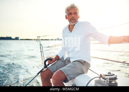 Lächelnd reifer Mann sitzen auf dem Deck des Schiffes genießen Sie einen sonnigen Tag Segeln auf dem offenen Ozean Stockfoto