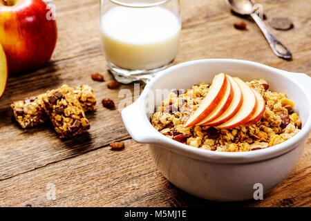 Gesundes Frühstück. Müsli mit Apfel, Rosinen, Müsliriegel und Milch Stockfoto