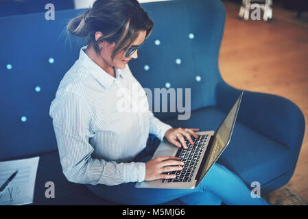 Lächelnden jungen Geschäftsfrau Brille sitzen auf einer Couch online arbeiten mit einem Laptop Stockfoto