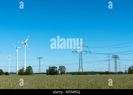 Freileitungen und Windkraftanlagen an einem sonnigen Tag in Deutschland gesehen Stockfoto