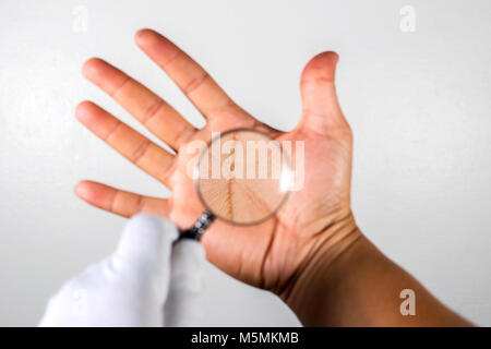 Ein Blick auf die Linien auf der Hand durch ein Vergrößerungsglas. Auf dem grauen Hintergrund. Stockfoto
