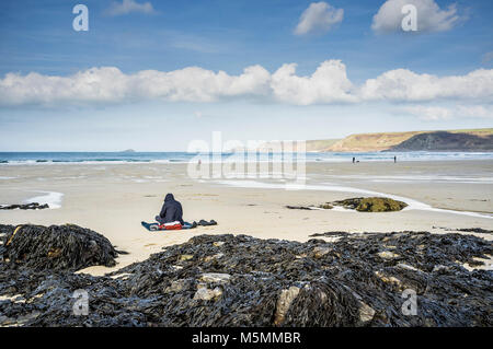 Eine vermummte Gestalt sitzen am Strand von Sennen Cove in Cornwall. Stockfoto