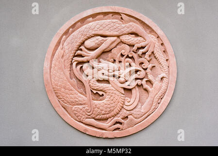 Rote kreisförmige dragon Flachrelief auf eine graue Wand, China Stockfoto