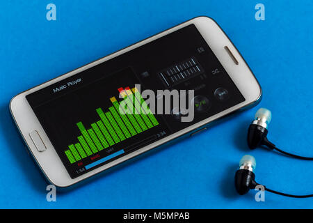 Music Player Equalizer auf dem Smartphone Display mit Kopfhörer, Nahaufnahme, blauer Hintergrund Stockfoto