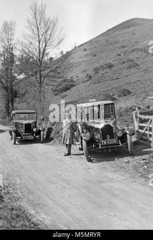 Modernen Schwarzen und Weißen 1920er Bild von zwei Oldtimer von der Seite eine kleine Straße in der Britischen Landschaft geparkt. Stockfoto