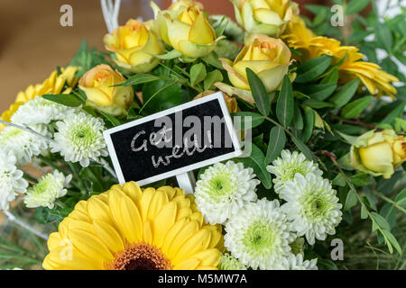 Blumenstrauß aus gelben und weißen Rosen, Lilien, Chrysanthemen und eine kleine Platine mit englischem Text: Gute Besserung Stockfoto