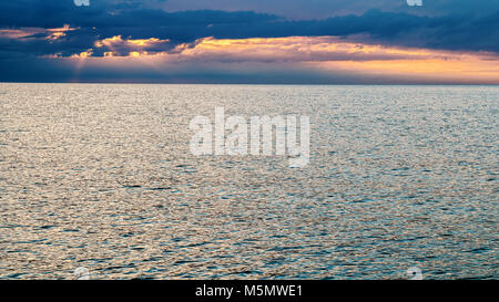 Dramatischer Sonnenuntergang Himmel über Meer. Sonnenstrahlen durch die Wolken. Sonnenuntergang über ruhige See mit sanften Wellen. Stockfoto