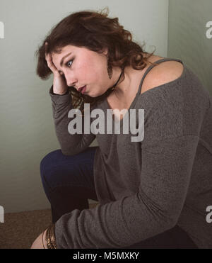 Junge Frau sitzend mit ihrer Hand zu ihrem Gesicht suchen umgekippt. Stockfoto