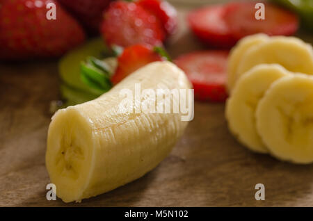 Bananen schälen und in Scheiben geschnittene Erdbeeren auf der Bodenplatte aus Holz Stockfoto