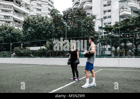 Erwachsene Frau training Muay Thai mit männlichen Trainer im grünen Feld mit Gebäude im Hintergrund Stockfoto