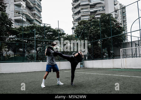 Erwachsene Frau training Muay Thai mit männlichen Trainer im grünen Feld mit Gebäude im Hintergrund Stockfoto