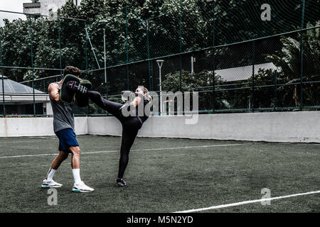 Erwachsene Frau training Muay Thai mit männlichen Trainer im grünen Feld mit Gebäude im Hintergrund Stockfoto