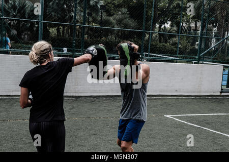 Erwachsene Frau training Muay Thai mit männlichen Trainer im grünen Feld mit Gebäude im Hintergrund Stockfoto