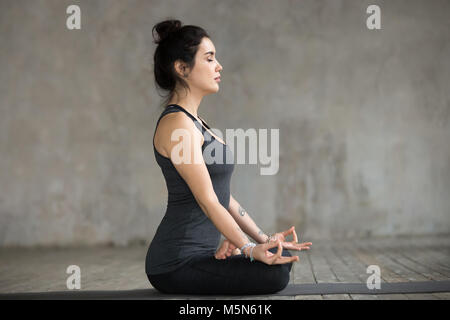 Junge sportliche Frau Üben Yoga, Sukhasana übung, einfach Sitz darstellen, arbeiten, tragen Sportswear, schwarze Hose und Top, Innen in voller Länge Stockfoto