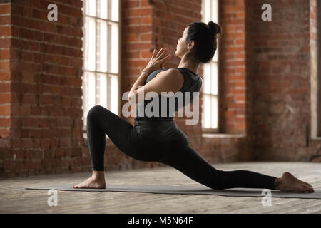 Junge sportliche Frau Üben Yoga, anjaneyasana Übung, Pferd Reiter darstellen, arbeiten, tragen Sportswear, schwarze Hose und Top, Innen- volle l Stockfoto