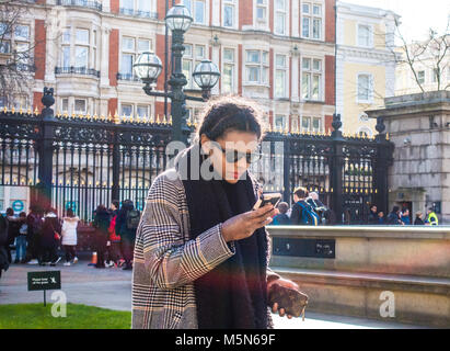 Chic Französin, Schal und Sonnenbrille an einem sonnigen Wintertag, mit ihrem Mobiltelefon außerhalb des British Museum, London, England, UK. Stockfoto