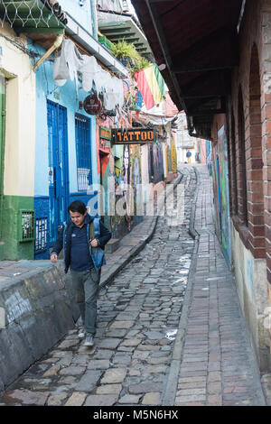 Ein Mann auf einem schmalen gepflasterten Straße in La Candelaria, der pulsierenden Herzschlag von Bogota mit einigen bunten Graffiti im Hintergrund Stockfoto