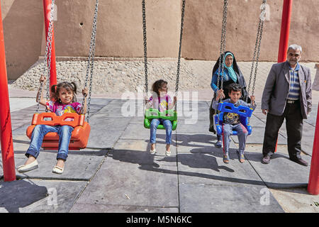 Kashan, Iran - 26. April 2017: Iranische Kinder Schwingen auf einer Schaukel, die Eltern sind, die dahinter stehen. Stockfoto