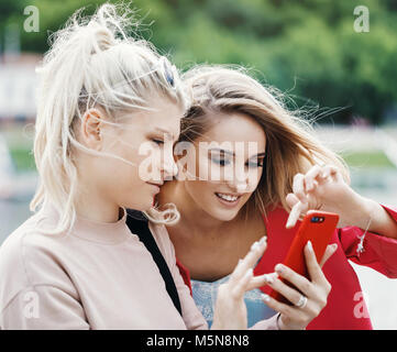 Zwei junge blonde Mädchen wählen Sie etwas in das Telefon. Close-up Stockfoto