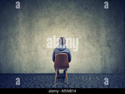 Rückansicht der Mann sitzt auf Stuhl vor Beton leere Wand erstellen Business Strategie zur Lösung eines Problems Stockfoto