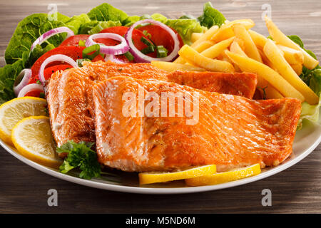 Gebratener Lachs mit Pommes frites und Gemüse auf hölzernen Tisch Stockfoto