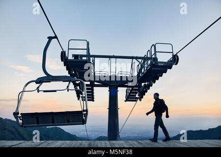 Touristische Mann am Ski Lift Station in Silhouette hoch in Mountain Ski Resort bei Sonnenaufgang Stockfoto