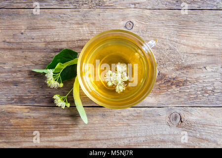 Gesunde pflanzliche linden Tee mit Bündel frische linden Blumen auf Holz- Hintergrund. Tasse organische linden Tee, Kräutertee trinken. Stockfoto