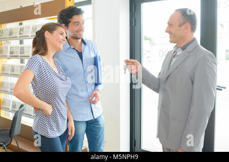 Immobilienmakler an junges Paar Schlüssel übergeben Stockfoto