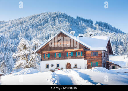 Panoramablick auf alte traditionelle Bauernhaus auf einem Hügel im malerischen Winterlandschaft Landschaft in den Alpen an einem schönen sonnigen Tag mit Blu Stockfoto