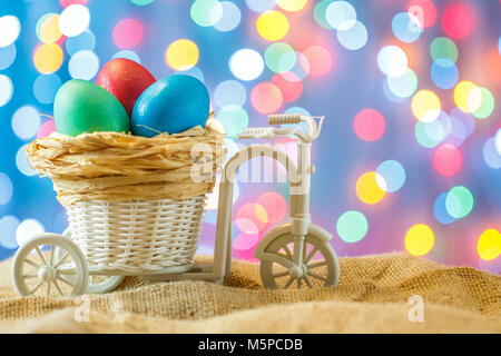 Ostern Karte, farbige Eier im Nest. Spielzeug Fahrrad mit einer Karre. Frohe Ostern. Blau bokeh Hintergrund. Spielzeug Fahrrad mit Warenkorb Stockfoto
