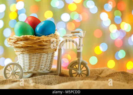 Ostern Karte, farbige Eier im Nest. Spielzeug Fahrrad mit einer Karre. Frohe Ostern. Gelb delikate bokeh Hintergrund. Stockfoto