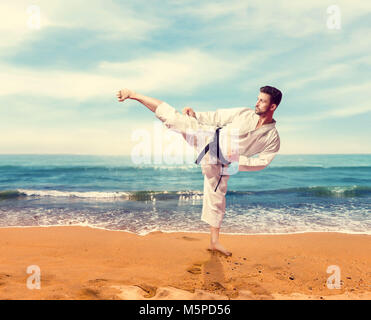 Martial Arts Kämpfer im weissen Kimono mit schwarzem Gürtel, Ausbildung an der Küste Stockfoto