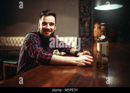 Lächelnd Mann an der Theke sitzen, Entspannung mit Alkohol. Happy Guy Spaß im Pub Stockfoto