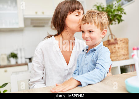 Glückliche Mutter küsst liebevoll ihren Sohn auf die Stirn in der Küche Stockfoto