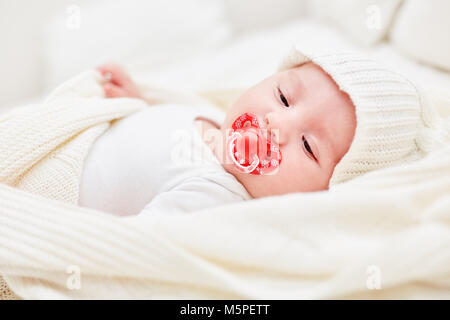 Baby mit Kappe und Schnuller liegend auf seinem Rücken zu Hause entspannt Stockfoto