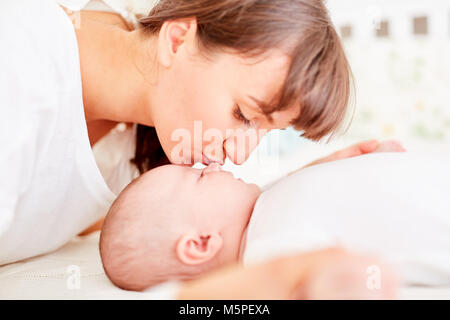 Junge glückliche Mutter gibt ihr Baby einen zärtlichen Kuss auf die Stirn Stockfoto