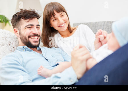 Glückliche Eltern liegen auf dem Sofa und spielen mit ihren kleinen Baby Stockfoto