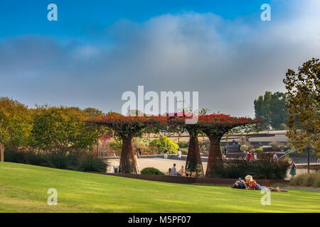 Ein paar liegen auf dem Rasen neben der Bougainvillea Lauben im Central Garden Plaza am Getty Center in Brentwood, Los Angeles, Kalifornien Stockfoto