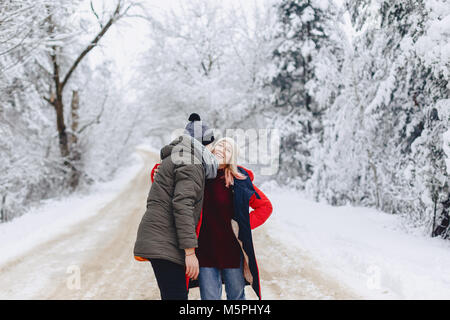 Eine schöne Familie Paar auf einem schneebedeckten Weg in den Wald und Umarmen, Küssen Stockfoto