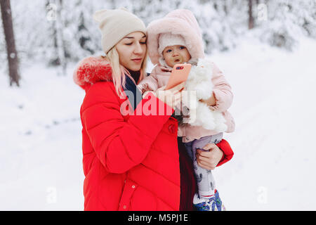 Mama hält das Baby in den Armen und macht die selfie in die verschneite Umgebung Spaß und Ausschreibung Stockfoto