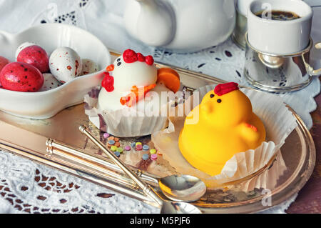 Figuren aus Marzipan in Form von weißen und gelben Hühner auf Ostern Tisch mit Kaffeetassen und Gebäck Eier in einem Ceramic White pot. Close Up. Stockfoto