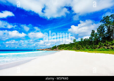 Granitfelsen, weißer Sand, türkises Wasser, blauer Himmel und Palmen am Paradise Beach auf den Seychellen, Petite Anse, La Digue Stockfoto