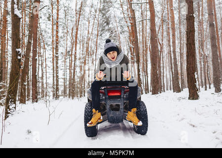 Ein Junge steht in der Nähe ein Quad in der Mitte eines verschneiten Kiefernwald Stockfoto