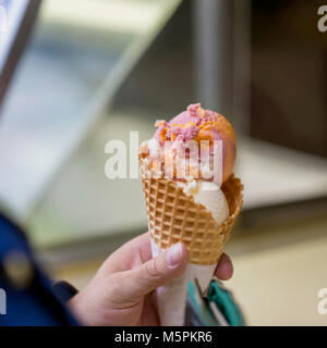 Vanille und Obst Eis mix im Waffle Kegel, weibliche Hand. Beliebte Köstlichkeiten für Erwachsene und Kinder. Selektive konzentrieren. Realen Szene Stockfoto