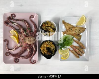 Gebratener Fisch, Reis mit Muscheln und Tintenfisch auf Teller mit Zitrone und Salat. Stockfoto