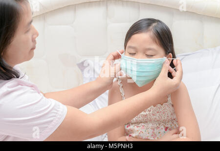 Mutter Verschleißschutz Maske Tochter gegen Grippe im Bett Zimmer zu schützen, Gesundheit und kranken Kind Konzept Stockfoto